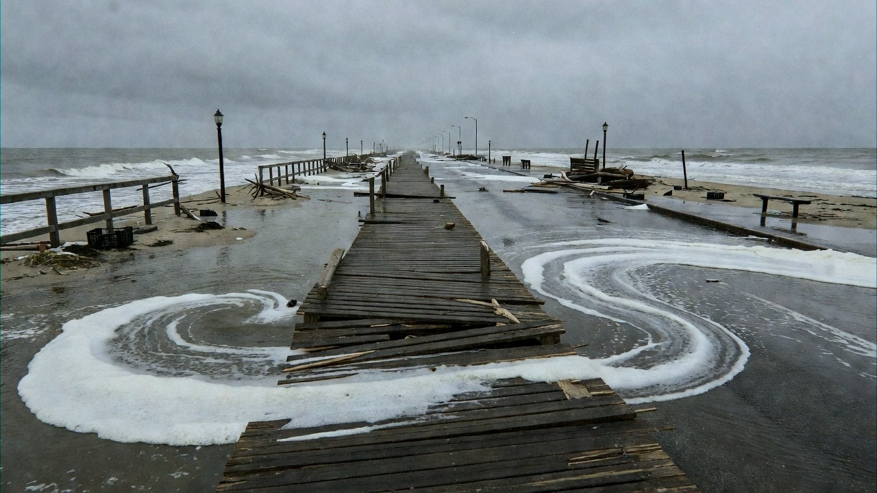 Seawater surging against a coastal boardwalk as a storm pushes waves toward beachfront homes